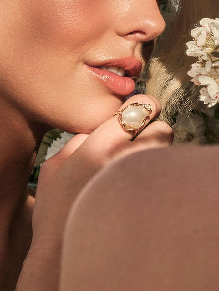 Close-up of a person wearing a gold ring with a pearl on a blurred background