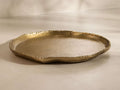 Angled view of the gold Aurelian Round Tray, showcasing an irregular, hammered texture rim and a smooth, matte finish.