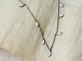 Australian Opal Drop Necklace with teardrop-shaped opals on an oxidized sterling chain, displayed on a beige fabric background.