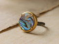 Autry Abalone Ring with iridescent oval abalone stone in 14k gold setting on oxidized silver hammered band, on light fabric.