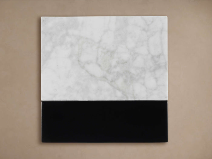Aviana Finish Board. A rectangular sample with a white marble top and a solid black bottom section, against a beige wall.