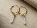 A pair of Ayla Moonstone Earrings with round gold vermeil hoops and teardrop moonstone pendants on a textured beige surface.