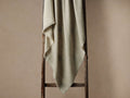Light gray Baby Alpaca Throw in Fog, with fringed edges, draped over a rustic wooden ladder against a neutral wall.
