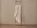 Light beige Baby Alpaca Throw with fringed edges draped over a rustic wooden ladder, against a warm beige wall and wood floor.