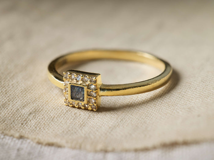 Close-up of a Gold Beatrice Ring with a square dark center stone surrounded by clear accent stones.