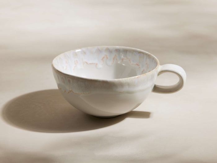 Bela stoneware mug, creamy off-white with reactive glaze showing subtle tan/pinkish marbling, handle on right.