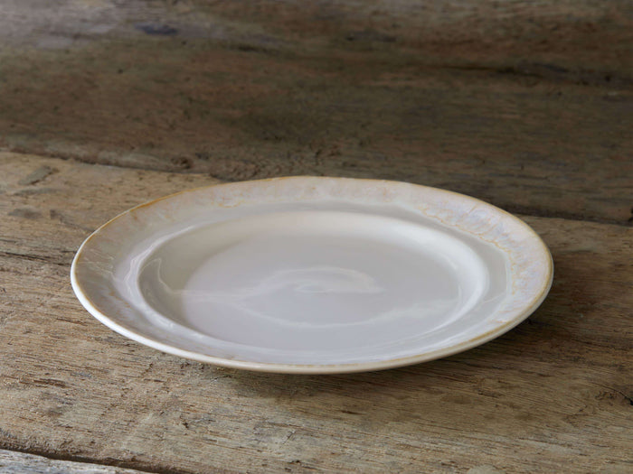 Bela Salad Plate, creamy off-white stoneware with glossy, antiqued rim, angled on rustic wood.