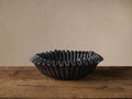 Black marble ruffle bowl with wavy edges, featuring natural grey tones, sits on a rustic wooden table against a light wall.