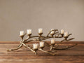 Antiqued brass Branch Candleholder, resembling tree branches, holding 8 lit votive candles in glass on a wooden table.