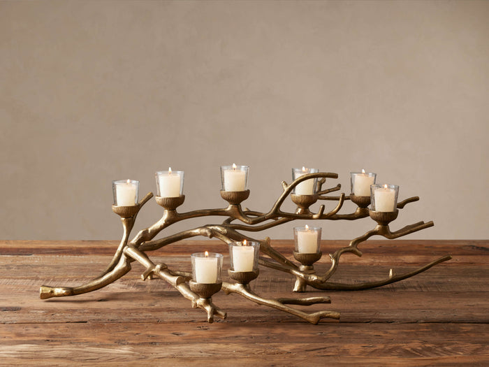 Antiqued brass Branch Candleholder, resembling tree branches, holding 8 lit votive candles in glass on a wooden table.