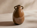 Bronwen Vase in brown tones, with a glossy finish, round body, two small loop handles near the top, on a light surface.