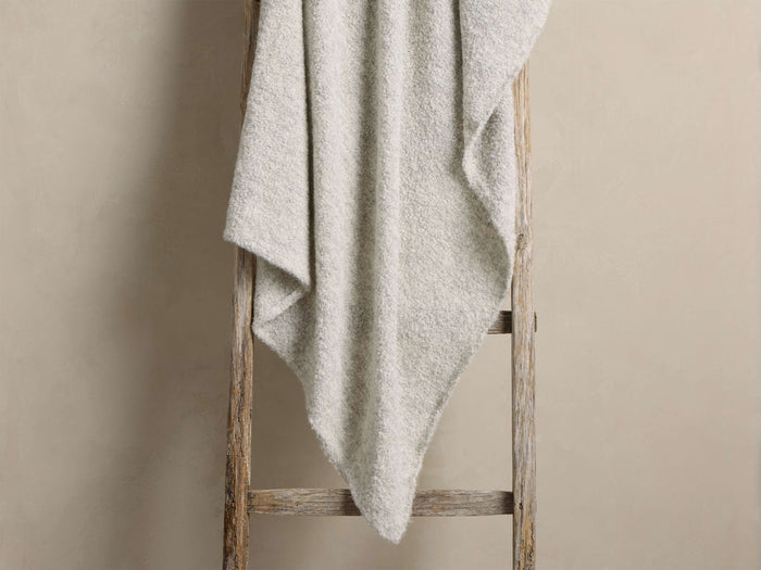 Light gray heathered blanket draped over a rustic wooden ladder, highlighting its soft, fluffy texture.