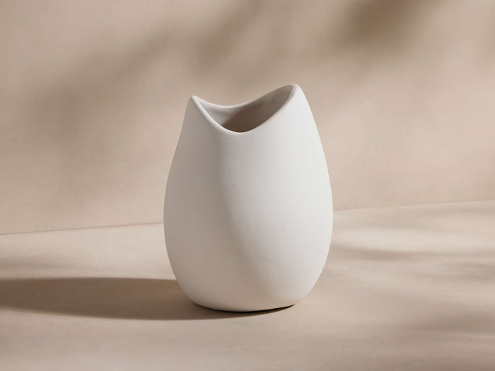 Calixta Bud Vase in matte plaster white, featuring an organic, fluid form with a rounded, slightly uneven rim, set on a beige background.