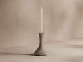 Calixta Candle Holder in matte taupe ceramic with a fluid, curved silhouette, holding a tall white taper candle.
