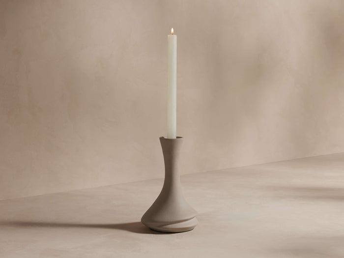 Calixta Candle Holder in matte taupe ceramic with a fluid, curved silhouette, holding a tall white taper candle.