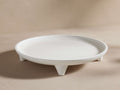 Calliope Round Tray in white with a textured surface, resting on three short legs, displayed on a neutral background.