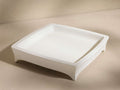 A square, off-white tray with slightly elevated edges and four short legs, set against a neutral background.