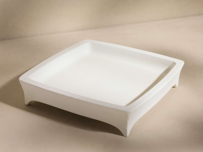 A square, off-white tray with slightly elevated edges and four short legs, set against a neutral background.
