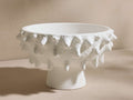 A textured, white ceramic bowl with a wide opening and a rough, spiked surface. The bowl stands on a short, circular base.