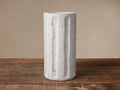 Light grey Cantera Vase, tall & cylindrical, with vertical hand-carved grooves, on rustic wood table.