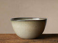 Canyon Cereal Bowl with earthy tan, brown speckles, and reactive greenish-brown glazed rim on a rustic wooden table.
