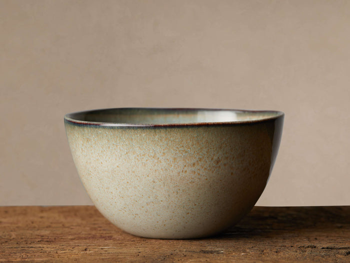 Canyon Cereal Bowl with earthy tan, brown speckles, and reactive greenish-brown glazed rim on a rustic wooden table.
