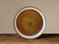 Round Canyon Dinner Plate with reactive brown, orange, cream, and gray glaze, sitting on a rustic wooden table.
