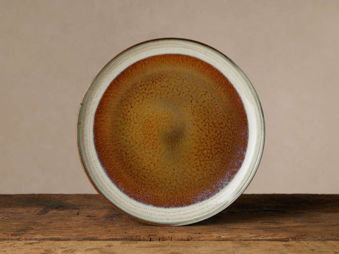 Round Canyon Dinner Plate with reactive brown, orange, cream, and gray glaze, sitting on a rustic wooden table.