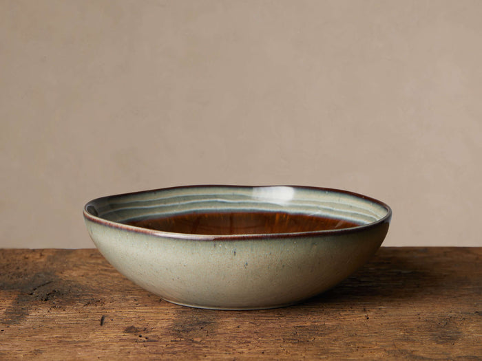 Canyon Pasta Bowl, light green/grey stoneware with glossy dark brown interior, blue/teal and white reactive glaze rim on wood.