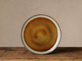 Single Canyon Salad Plate, round, with a reactive amber, gold, brown swirling glaze and a greyish-white rim, on wood.