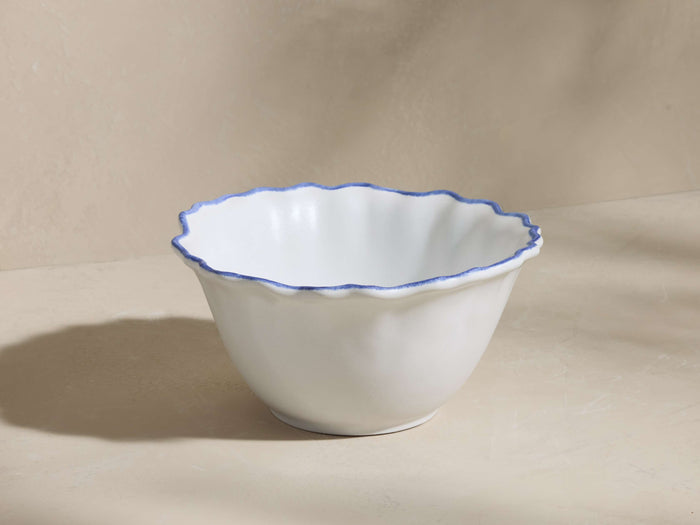 White ceramic Capuchos Cereal Bowl with a wavy rim, hand-painted with blue edging, on a light background.
