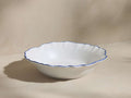 Capuchos Pasta Bowl: White matte ceramic stoneware bowl with a wavy, hand-painted blue rim, angled on a light surface.