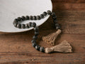 Carved Wooden Strand with hand-carved black mango wood beads and jute rope, featuring tassels, displayed on wooden table.