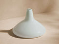 Cassia Flat Vase: Hand-blown, pale green glass with a wide, flat base tapering to a narrow neck on a beige background.