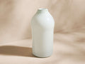Cassia Tall Bottle Vase, opaque light green glass, cylindrical base tapering to a narrow top, standing on a light surface.