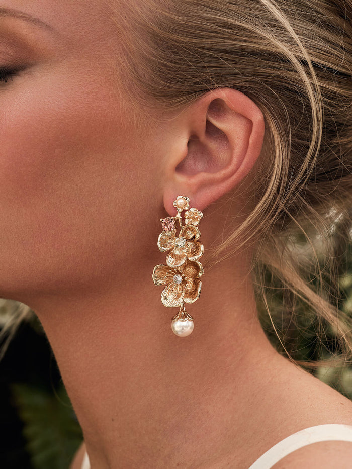 Close-up of a woman wearing gold floral earrings with a blurred natural background