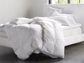 Chamber Pillow Insert on a neatly made bed with a white duvet, surrounded by other pillows, in a bright room with soft lighting.