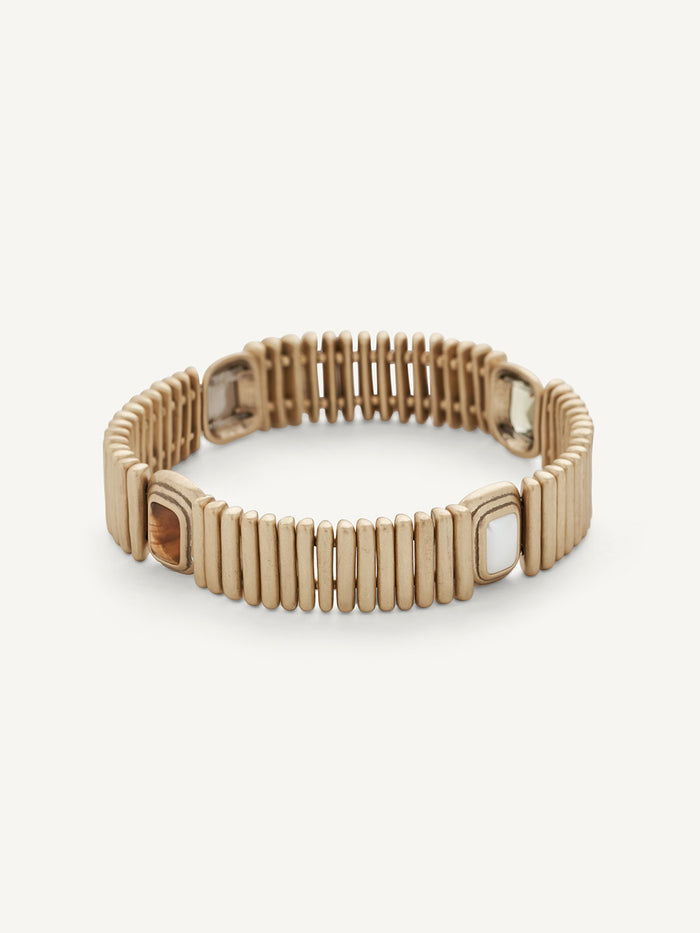 A gold-toned metal bracelet with a segmented, ribbed design and rectangular links, shown on a light off-white background.