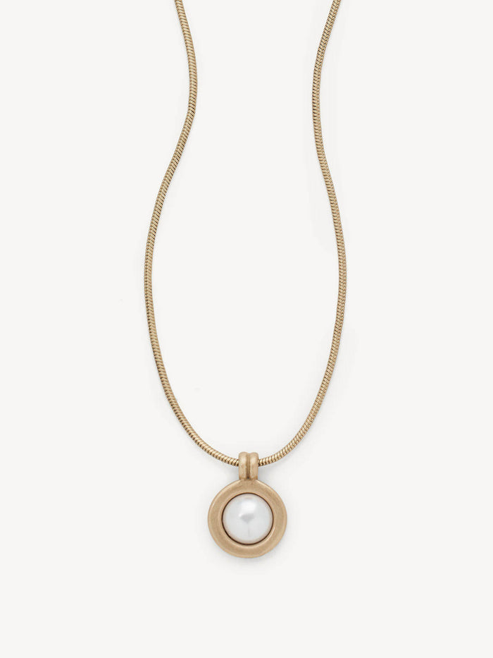 A gold snake chain necklace with a circular pendant featuring a white pearl in the center, set against a clean off-white background.