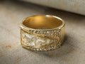 Close-up of the gold Clairen Ring, a wide band featuring a shimmery white and gold textured center, flanked by two rows of small clear stones.
