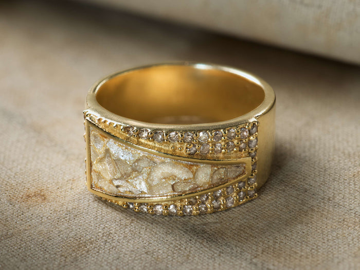 Close-up of the gold Clairen Ring, a wide band featuring a shimmery white and gold textured center, flanked by two rows of small clear stones.