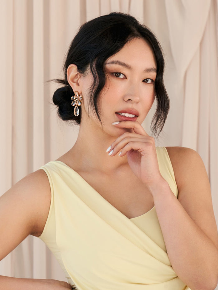 Woman wearing floral earrings and a yellow dress with a neutral background