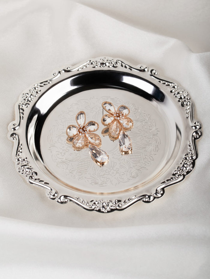Gold earrings on a decorative silver tray with intricate designs on a white fabric background