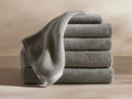 A stack of five plush, gray towels neatly arranged with one draped over the top, set against a beige background.