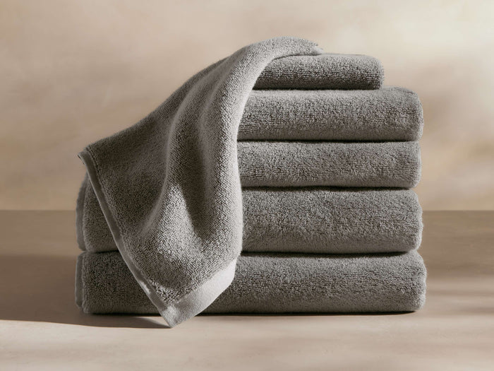 A stack of five plush, gray towels neatly arranged with one draped over the top, set against a beige background.