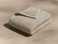 A folded beige towel lies on a smooth surface with a neatly turned-over edge, highlighting its soft, plush texture.