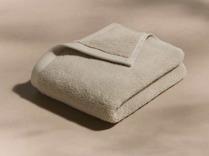 A folded beige towel lies on a smooth surface with a neatly turned-over edge, highlighting its soft, plush texture.