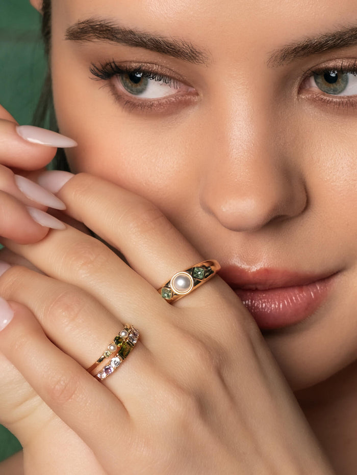 Close-up of a woman's hand wearing a ring with a pearl and green gemstones.