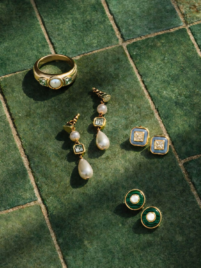 Gold jewelry set with earrings, ring, and brooch on a green tiled surface
