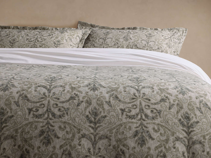 Front view of the Corinne Duvet with a grey-green damask-inspired motif and two matching pillows, over white sheets.